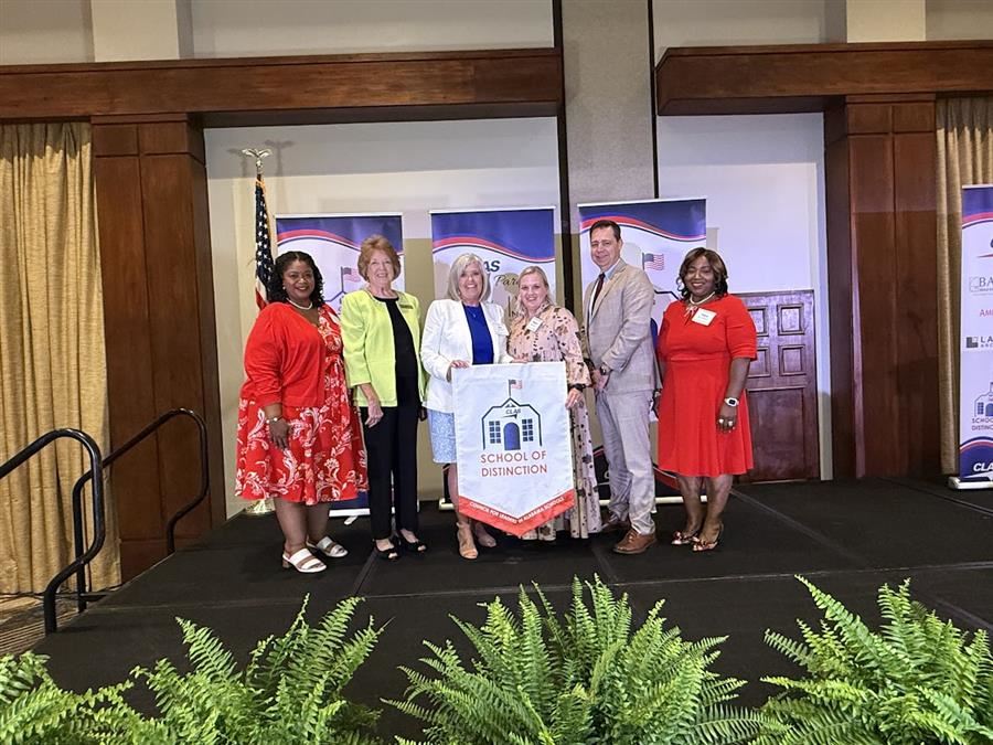  Six people stand on stage holding a "School of Distinction" banner at an awards event, smiling.